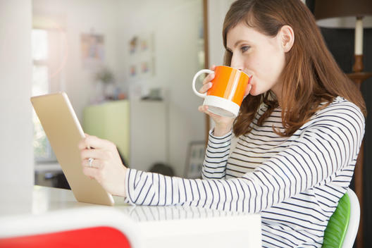 Woman Drinking Coffee and Using Digital Tablet at Home