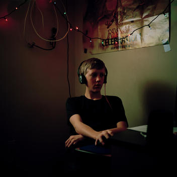 Portrait of a young introverted, reclusive teenage boy wearing headphones sitting in a dark bedroom spends countess hours on the computer playing games on Facebook. Pleasant Grove, Utah