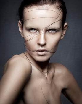 Studio beauty cropped portrait of a caucasian brown hair blued eyed female model with string and snaps on her face, artistic, bright light, desaturated color palette