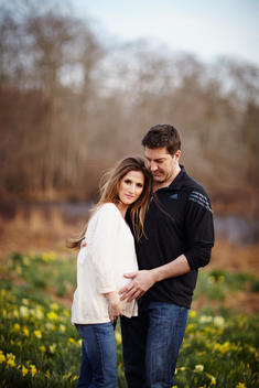Pregnant woman holding her belly with her husband standing in a field in the afternoon.