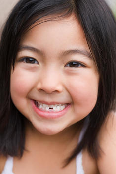 Close up of young Asian girl smiling with tooth missing