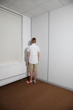 School boy standing in the corner of the classroom.
