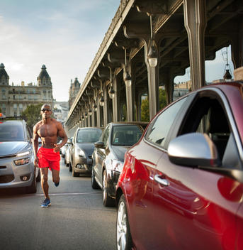 African athletic man running amidst traffic in European city, Bir-Hakeim Bridge in background