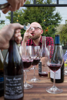 a man drinking from a red wine glass at an outdoor table covered with wine glasses and bottles at the South East Wine Collective