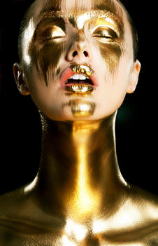 model painted partially with gold Make up in her face and down her chest in front of a black back ground