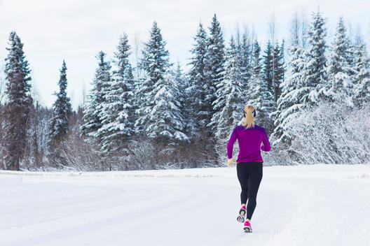 Adult female runner listening to music during her run on snow covered road.