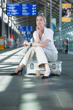 Germany, Leipzig-Halle, Young woman in Airport departure lounge, sitting on suitcase