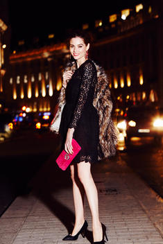 Model on city street at night wearing a black dress and pink clutch