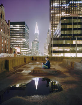 woman meditating on the top of a roof in New York City at night (Chrysler building)
