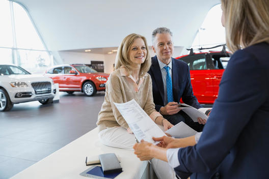 Saleswoman and couple finalizing paperwork in car dealership