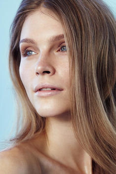 Close-up up of dark blonde model in bare skin and light natural makeup against light blue background