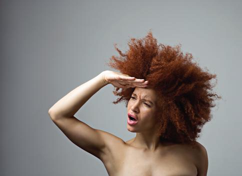 Mixed race woman with ginger hair in studio in front of grey background.