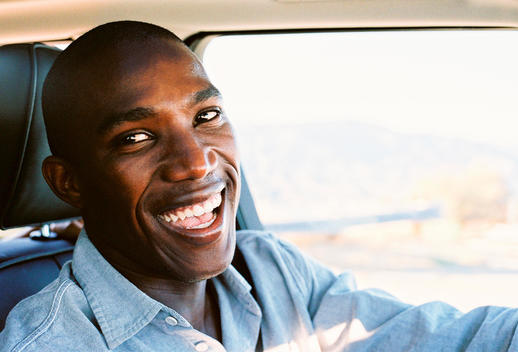 Portrait of young smiling African American man driving car and looking at camera