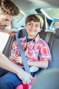 Father fastening seat belt for boy in back seat of car