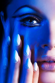 close up of a face with white nails decorated with crystals, photographed with long time exposure in colored blue light and strobe, for Nail it Magazine