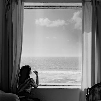 Woman sitting in front of window staring at the sea
