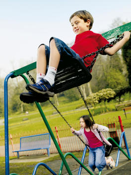 Boy And Girl Playing On Playground Swings.