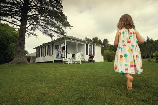 Young girl walking towards rustic lake cabin in Vermont wearing summer dress.
