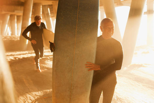 Older surfers carrying boards under pier