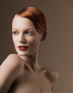 Studio beauty tight crop portrait of a red haired blue eyed female model in dark red lipstick, she looks over her shoulder off camera, hair is pulled back