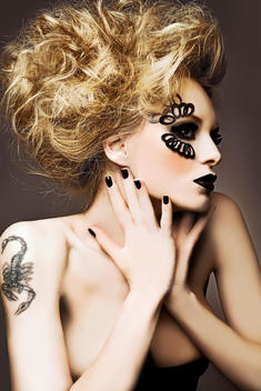 Fashion model with volume hair and dark makeup in a gothic style. There is a scorpion tattoo on her shoulder.