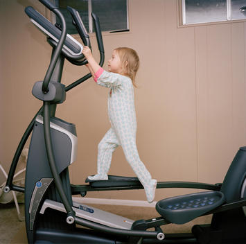 A young blonde girl wearing blue heart pajamas play runs on her mother\'s large running machine