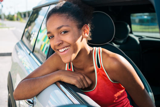 Young black girl with Afro is having fun while looking outside of a sports car