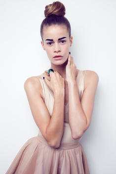 fashion model in studio, wearing a nude colored ballerina outfit and green ring with strong eyebrows and hair in a top bun