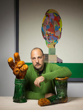 Art dealer, Stefan Simchowitz sits at a table in his home resting his arms on piece of sculpture