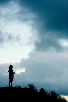 One young female girl in silhouette watches the sunset with a large sky at Bethells Beach, Auckland, New Zealand