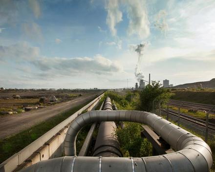 Steel pipes snaking in foreground and traveling deep into the distance in brown field industrial fields.