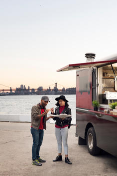 A young man and woman ordering pizza from a Food Truck with Manhattan in the background