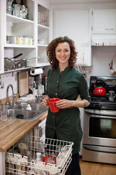 A Woman Puts Away The Dishes In Her Kitchen.