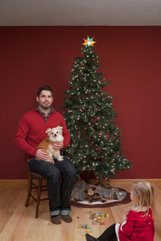 A man poses for a Christmas portrait with his dog and daughter.