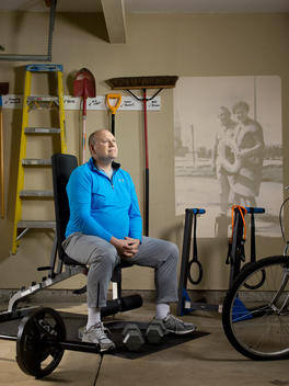 A man sits on an exercise machine in his garage with an old family photo projected on the wall behind him