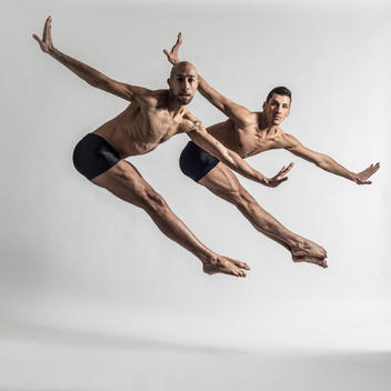 White male dancers in coordinated duo jazz jump against a white background