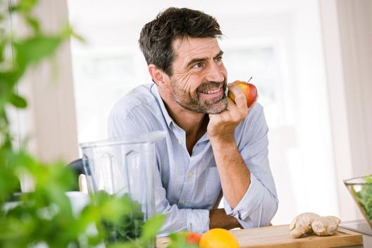 Mature man eating apple at kitchen counter