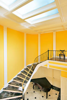 View From Interior Balcony Looking Over Yellow Atrium With Marble Stairs, Grand Piano, All Covered By Massive Skylight