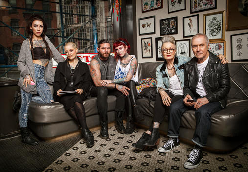Group portrait, showing generations and tradition in tattoo art and lifestyle. Two tattooed seniors sit with four young tattooed adults in a tattoo shop.