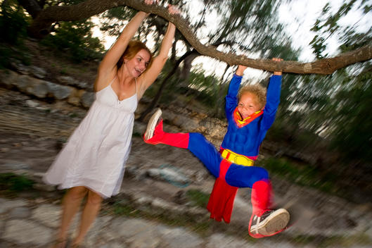 Boy dressed in a costume swinging from a tree branch with his mother, Austin, Texas, USA.
