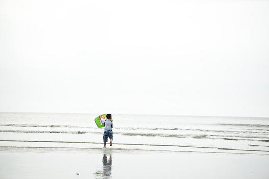 Little Boy Running Towards The Sea With A Boogie Board