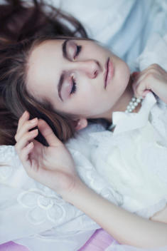 Young adult female with long blonde hair resting with eyes closed wearing pearl necklace