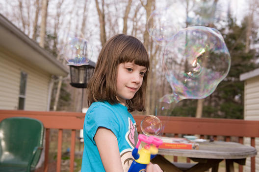 Young Girl Playing With A Bubble Gun Outside On A Deck