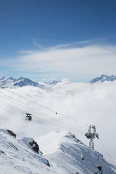 view of ski lift gondal reaching the top of the mountain above the clouds