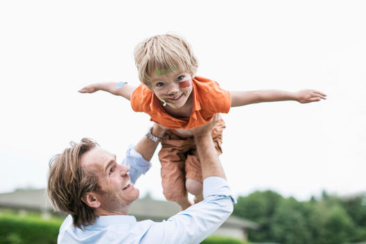 Playful father lifting injured son against clear sky
