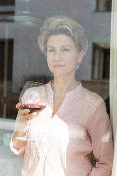 Portrait of mature woman with red wine glass looking out of the window
