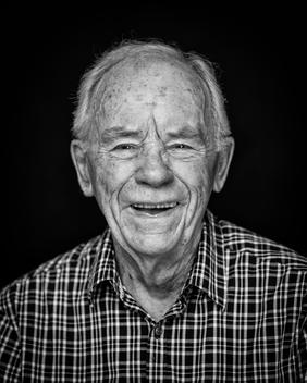 Black and white portrait of elderly man wearing a plaid shirt smiling
