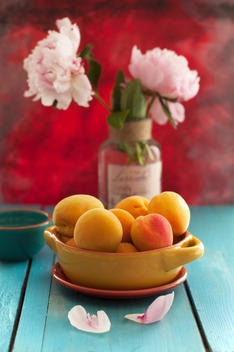 Bowl of apricots with peonies flowers on wooden table