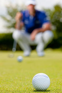 golf ball on green, with crouching golfer out of focus in background