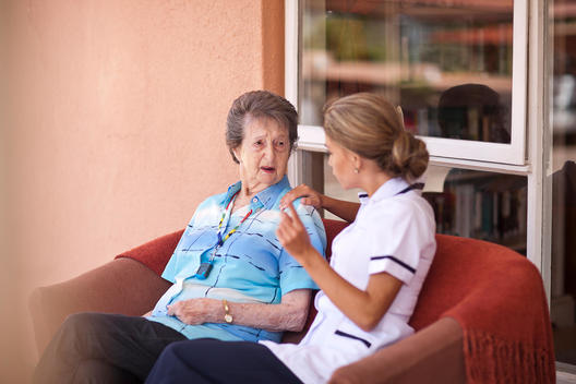 Care assistant chatting to senior woman on sofa